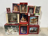 Full lot showing stacked boxes of vintage Christmas village porcelain houses, lighted ship, carousel, church, lighthouse, and fiber optic village scene.