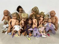 Photo showing full lot of 15 vintage baby dolls of various styles and sizes, some with rooted hair, some molded, some with attached clothing including pajamas and dresses.