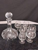 Photo showing Atlantis crystal liquor decanter alongside 6 snifter glasses on black cloth.