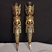 Pair of wooden Balanese prince and princess sculptures with gold and green paint against black background