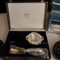 Opened Caviar House box showing glass condiment dish with silver handles and two silver serving utensils wrapped in plastic.