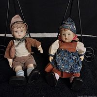 Front view of Hanzel and Gretel porcelain dolls sitting against black background, showing detailed clothing and expressions