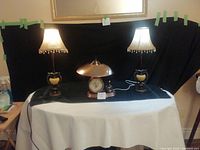 Wide shot of two vintage lamps flanking a dome-topped clock and a small carousel music box on black cloth.