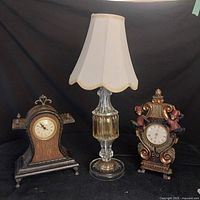 Front view of the MCM glass lamp with original shade flanked by two vintage clocks: a traditional wood clock and a monkey-themed ornate clock.