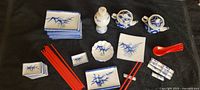 Full view of sushi serving set items arranged on black fabric. Contains various blue and white dishes with bamboo painting, red chopsticks, chopstick holders, soy sauce dishes, and wrapped white soup spoons.