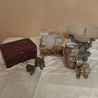 Overall view of the collection showing the wooden box, carved elephant frame, three elephant figurines, ceramic vase, and elephant bowl.