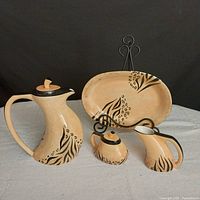 Photo showing full set of 6 pottery pieces including coffee pot, sugar bowl, creamer, serving platter and stand on white cloth with black background.
