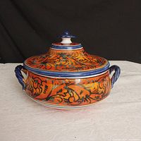 Front view of vintage Sicilian ceramic bowl with lid showing orange floral pattern with blue handles and knob lid.