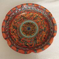 Top view showing detailed hand painted floral and geometric patterns in orange, green, and blue with scalloped rim detail.