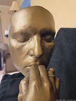 Close-up of the face portion of the bronze-colored sculpture showing closed eyes and detailed facial features.