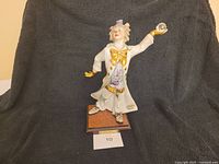 Full view of the porcelain clown figurine in costume standing on brown base with signature plaque.