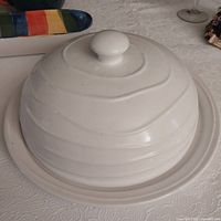 White ceramic platter with ripple dome cover photographed from side angle on table.