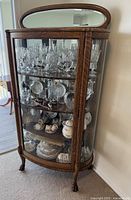Front and slight side view of wooden curio cabinet showing glass front door, interior glass shelves and mirrored top panel