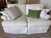 Front view of white slipcovered loveseat with cushions and throw pillows