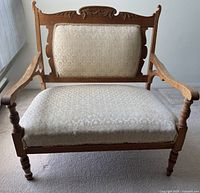 Front view of wooden wider love seat with patterned cream upholstery and carved wood detailing on backrest and arms.