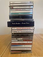 Tall stack of 27 CDs showing some spine titles including Nick Drake 'Fruit Tree', Leonard Cohen 'The Future', Adele '25', The Police 'Greatest Hits', George Michael 'Ladies & Gentlemen'
