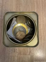 Overhead view into open gold-tone square tin showing mixed loose coins and coin holders