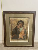 Front photo of framed religious art showing Madonna and child in traditional style with dark wooden frame and beige mat.