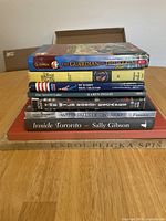 Stack of seven books on tabletop showing titles The Guardian of the Realm, The Ultimate Trivia Collector, The Secret Lake, Firefly, Waterfalls of Ontario and Inside Toronto by Sally Gibson, plus other book in foreign language and red cloth bound book.