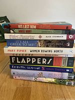 Stack of 11 books showing titles and authors on spines including His Last Bow, Whose Body?, Without Reservations, It's All Greek to Me!, Women Rowing North, Break of Day, Flappers, Eccentric Glamour, She Shoots to Conquer, Withering Heights