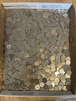 Top-down view of a large batch of Canadian coins in a box, showing many quarters and smaller denominations, several with visible red poppy markings.