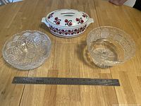 Top down view of the three items showing the casserole dish with lid centered and two glass bowls on either side, ruler indicating size.