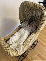 Doll resting in wicker stroller showing full outfit and stroller design