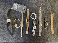 Seven vintage wristwatches arranged on a black cloth surface showing variety in strap materials, case shapes, and dial styles.