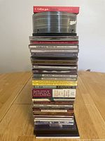 Stacked CDs showing spines and some visible titles in cases, with a Czech phrasebook on top and some discs without cases at the very top.