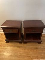 Pair of mahogany nightstands with two drawers each, placed side by side on hardwood floor against a wall.