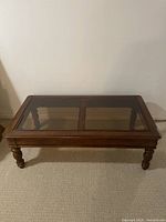 Full view of the rectangular coffee table with a glass top inset into a polished brown wooden frame and four carved legs.