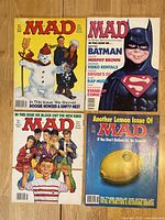 Four different Mad Magazine covers from the 1980s-1990s with vintage pop culture satire themes and characters shown on a wood surface.