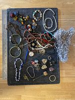 Full assortment of costume jewelry including various necklaces, bracelets, earrings, pins, and brooches laid out on gray fabric with a ruler for scale