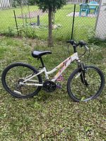 Full side view of white Nakamura Pristine hybrid bike on grass with chain, gears, tires and frame visible.