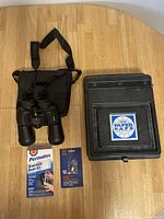 Full set from top perspective showing all items: Nikon binoculars with case, black film paper safe box, Permatex windshield repair kit, and 12V bulb.