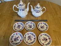 Two fine bone china teapots and six matching saucers arranged on a wooden table with a ruler for size reference.