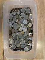 Top view of a plastic bin filled with mixed coins in various materials and sizes.