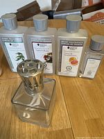 Photo showing La Berger home fragrance liquid bottles in eucalyptus, heavenly spruce, grapefruit scents, along with a clear glass diffuser bottle with metal top.