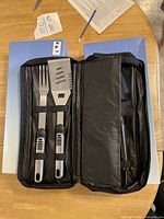 BBQ utensil set inside an open zippered black carrying case showing fork and slotted spatula