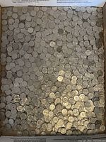Top down view of a large quantity of loose US dimes in a box.