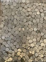 Close-up view of a large pile of mixed US nickels showing Jefferson and Buffalo nickel designs, loosely spread on a flat surface.