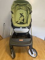 Front view of green STOKKE stroller showing padded seat and safety harness.