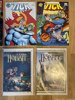 Photo of 2 The Tick comic books and 2 The Hobbit comics featuring illustrated covers.