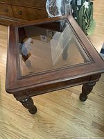 Top angled view showing dark brown wooden frame with beveled glass inset and carved legs on hardwood floor.
