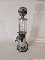 Full view of the vintage style chrome alcohol dispenser with clear measuring cylinder and round top.