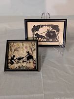 Two antique silhouette artworks in small black frames, showing a horse-drawn carriage and a garden scene with woman and child.