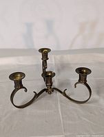 Front angled view of the brass three-arm candle holder showing curved arms and tarnished brass finish.