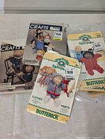 Four vintage paper sewing patterns for making Cabbage Patch Kids doll clothes, showing original wrappers with images of dolls in various outfits.