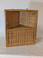 Front view of the natural wicker corner shelf with a hinged door on the lower section.