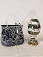 Photo showing black and white marbled glass purse sculpture and decorative green and white egg figurine with gold accents on pedestal base.